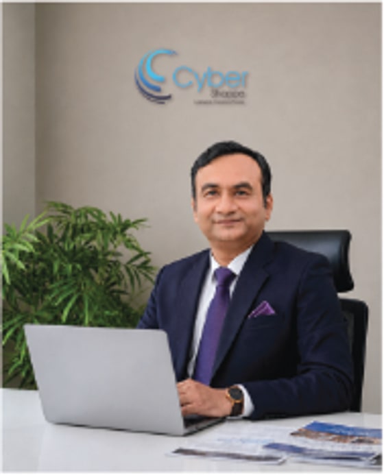 Portrait of a Cyber Shoppe founder at his desk, the company logo on the wall behind him