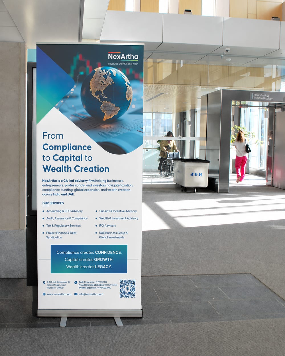 NexArtha roll-up standee in an office lobby, headed From Compliance to Capital to Wealth Creation